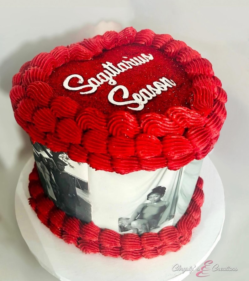 May include: A round cake with red frosting and the words "Sagittarius Season" in white. The cake has a white base with black and white photos wrapped around it. The cake is on a white cake board.