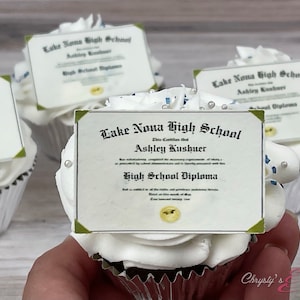 May include: Four white cupcakes with white frosting and a blue and green graduation diploma topper that says "Lake Nona High School" and "High School Diploma".