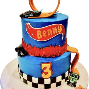 K&ouml;nnte beinhalten: Eine zweist&ouml;ckige blaue Geburtstagstorte, die mit einem Hot Wheels-Thema verziert ist. Die Torte hat eine rote und orangefarbene Hot Wheels-Bahn, ein schwarzes Spielzeugauto und ein rotes Banner mit dem Namen "Benny". Die untere Schicht hat ein kariertes Muster und die Zahl "3" in Gelb. Die Torte steht auf einem wei&szlig;en Tortenst&auml;nder mit den Worten "Happy Birthday" in Orange.