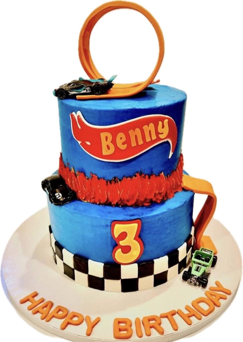 K&ouml;nnte beinhalten: Eine zweist&ouml;ckige blaue Geburtstagstorte, die mit einem Hot Wheels-Thema verziert ist. Die Torte hat eine rote und orangefarbene Hot Wheels-Bahn, ein schwarzes Spielzeugauto und ein rotes Banner mit dem Namen "Benny". Die untere Schicht hat ein kariertes Muster und die Zahl "3" in Gelb. Die Torte steht auf einem wei&szlig;en Tortenst&auml;nder mit den Worten "Happy Birthday" in Orange.