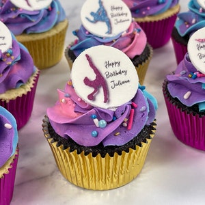 May include: A close-up of cupcakes decorated with purple, pink, and blue frosting. Each cupcake has a round edible image on top with a gymnast silhouette and the text "Happy Birthday Juliana".