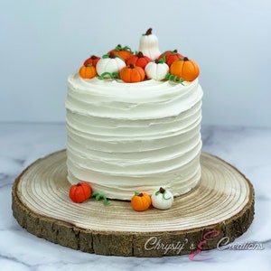 May include: A white frosted cake decorated with orange and white fondant pumpkins. The cake is on a wooden cake stand.