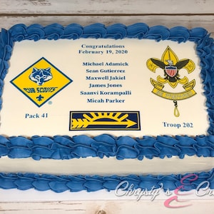 May include: A white rectangular cake decorated with blue frosting. The cake has a printed image of the Boy Scouts of America logo, a Cub Scouts logo, and a patch with a sun and arrow. The cake also has the text "Congratulations February 19, 2020" and a list of names. The cake is labeled "Pack 41" and "Troop 202".