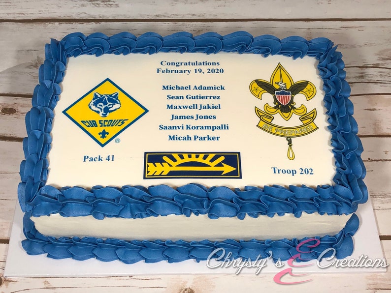 May include: A white rectangular cake decorated with blue frosting. The cake has a printed image of the Boy Scouts of America logo, a Cub Scouts logo, and a patch with a sun and arrow. The cake also has the text "Congratulations February 19, 2020" and a list of names. The cake is labeled "Pack 41" and "Troop 202".