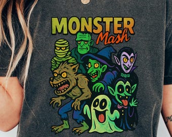 May include: Dark grey t-shirt with a vibrant cartoon monster graphic and the text "MONSTER Mash". The design includes a werewolf, mummy, and vampire. The shirt has a relaxed fit and short sleeves.