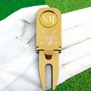 May include: Gold golf ball marker and divot tool with the initials "NM" and the name "Nora Mitchell" engraved on it.
