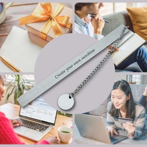 May include: Silver bookmark with a chain and a round charm. The bookmark is engraved with the text "Create your own sunshine".