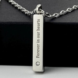 May include: Silver necklace with a vertical bar pendant engraved with the words "Forever in our hearts" and a small diamond accent.