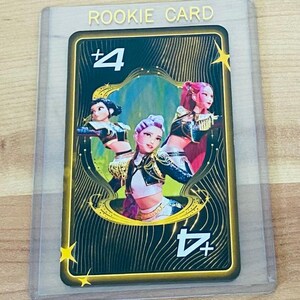 May include: A collectible trading card encased in a clear plastic sleeve, labeled ROOKIE CARD at the top. The card features a black background with gold wavy lines, a central illustration of three figures, and the text +4 in the corners.