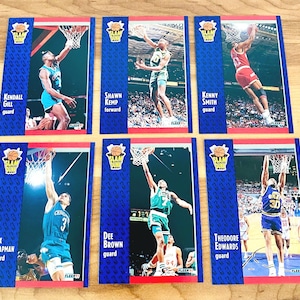 Puede incluir: Seis cromos de baloncesto vintage con jugadores de la NBA en acci&oacute;n. Cada cromo tiene un borde azul con las palabras "SLAM DUNK" y el nombre y la posici&oacute;n del jugador. Los cromos muestran a jugadores como Kendall Gill y Shawn Kemp.
