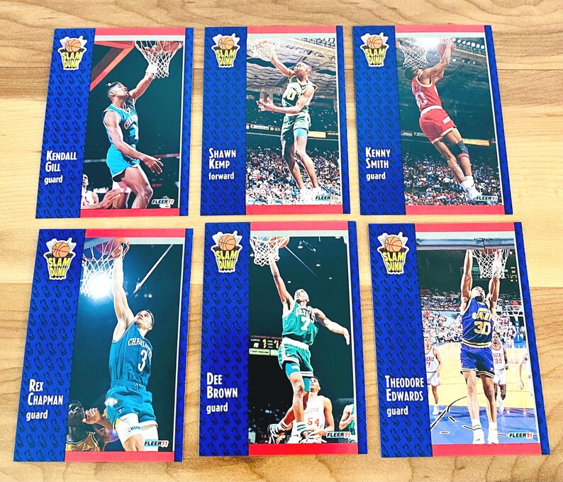 Puede incluir: Seis cromos de baloncesto vintage con jugadores de la NBA en acci&oacute;n. Cada cromo tiene un borde azul con las palabras "SLAM DUNK" y el nombre y la posici&oacute;n del jugador. Los cromos muestran a jugadores como Kendall Gill y Shawn Kemp.