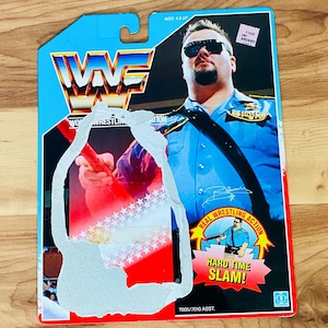 May include: A vintage WWF action figure of The Big Boss Man in a blue police uniform. The packaging features the WWF logo, the words "Real Wrestling Action," and "Hard Time Slam!" The figure is for ages 4 & up.