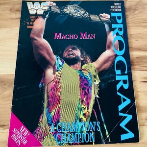 May include: A wrestling magazine cover featuring a wrestler holding a championship belt above his head. The wrestler is wearing a colorful, patterned vest and has long, curly hair. The cover text reads "Macho Man" and "A Champion's Champion".