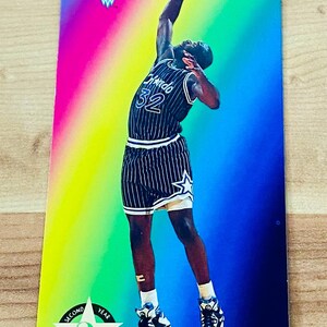 May include: A basketball trading card featuring Shaquille O'Neal in an Orlando Magic uniform, number 32. The card has a colorful background with the text "NBA JAM SESSION" and "'93-'94". The bottom of the card has the text "SHAQUILLE O'NEAL".