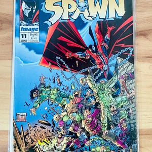 May include: A comic book cover featuring the character Spawn, a red and black superhero with a skull on his chest, fighting a group of soldiers. The cover is titled "Spawn" and is issue number 11. The comic book is published by Image Comics.