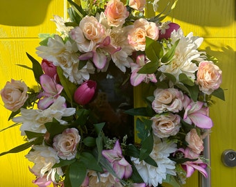 May include: A pink and white floral wreath with green leaves hangs on a bright yellow door.