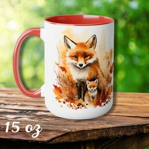May include: White 15 oz ceramic mug with a red interior and handle. The mug features a watercolor illustration of a mother fox and her cub surrounded by autumn leaves. The fox has orange and white fur.