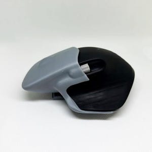 Puede incluir: Un ratón de ordenador negro con un agarre ergonómico gris adjunto. El ratón tiene una rueda de desplazamiento y un diseño curvo para un uso cómodo. El agarre gris parece estar impreso en 3D.