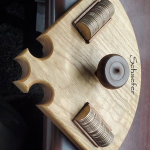 Puede incluir: Portamonedas de madera con tres ranuras para monedas. El portamonedas tiene una parte superior marrón oscuro con la palabra "Schaefter" grabada. El portamonedas está hecho de madera clara con veta natural.