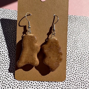 May include: A pair of brown sugar cookie-shaped earrings with silver hooks. The earrings are on a brown card.