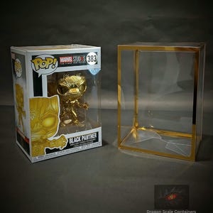 Puede incluir: Una figura Pop! de Pantera Negra de color dorado en su caja original, junto a una vitrina transparente con ribetes dorados. La caja tiene el logo de Marvel Studios y el número 383.