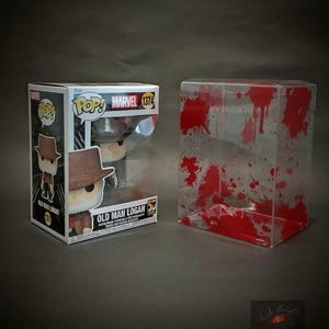 May include: A Pop! Vinyl figure of Old Man Logan from Marvel Comics. The figure is in a clear plastic protector with red blood splatter. The figure is wearing a brown hat, brown jacket, and blue jeans. The figure is holding a pair of claws. The box is white with red and black accents. The box has the words "Pop!" and "Marvel" on it. The box also has the number "1374" on it.