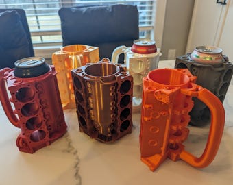 Puede incluir: Cinco tazas impresas en 3D con forma de bloques de motor en diferentes colores: rojo, naranja, marrón, dorado y blanco. Las tazas están diseñadas para contener una lata de bebida.