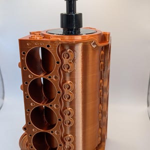May include: A copper-colored 3D printed soap dispenser shaped like an engine block. The dispenser has a black pump on top.