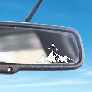 May include: White car rearview mirror with a white mountain range and five stars sticker on the glass.