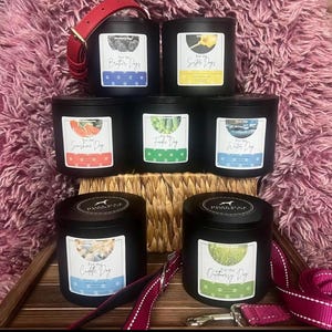 Puede incluir: Un conjunto de velas negras con etiquetas variadas, incluyendo "For the Brother Dogs" y "For the Sister Dogs". Las velas están dispuestas sobre una bandeja de madera, con un collar y una correa rojos para perros.