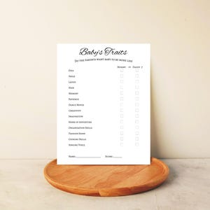 May include: A white baby shower game card titled "Baby's Traits" with a list of traits and check boxes. The card is on a wooden tray. The text includes "Mommy or Daddy?" and "Name: Score:"