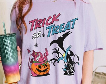 May include: A light purple t-shirt featuring the text "TRICK OR TREAT" in pink and blue, with two small spiders hanging from the text. Below, a pink devil character sits in a jack-o'-lantern, next to a black and blue skeletal creature.