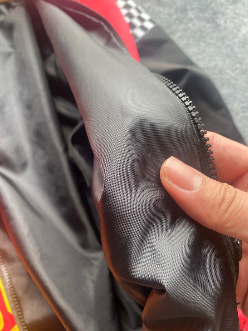 May include: Close-up of the black lining inside a red and black jacket. The lining is smooth and has a subtle sheen. A zipper is visible along the edge of the lining.