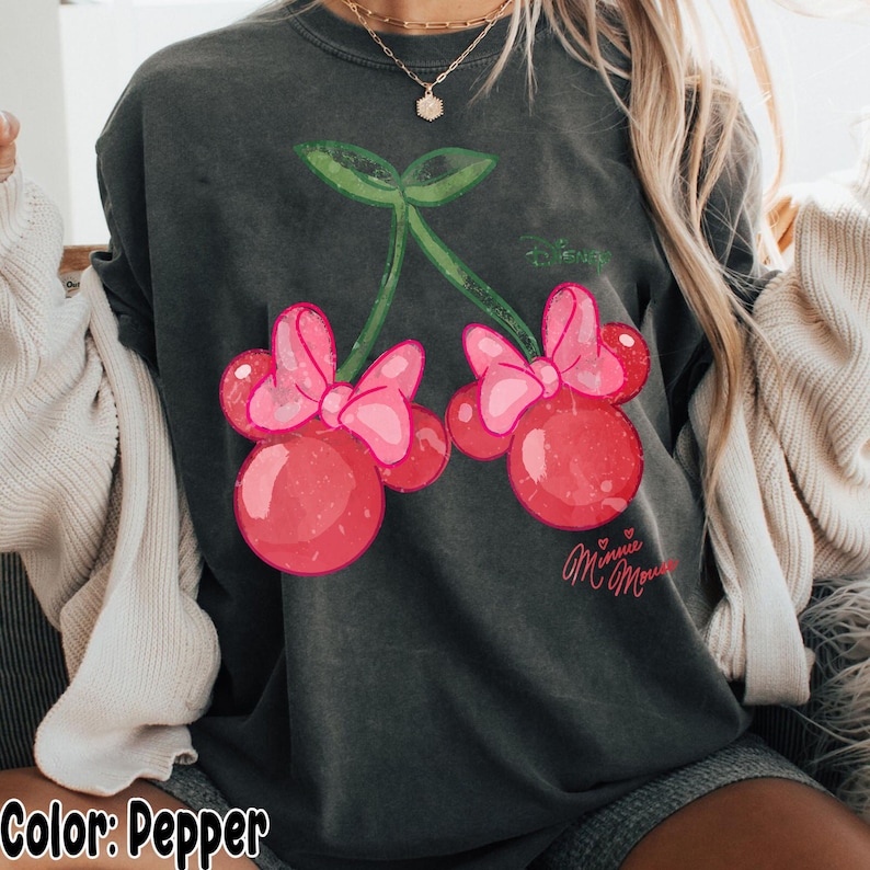 Op de afbeelding: Donkergrijze sweatshirt met een kersendesign met roze strikken en Minnie Mouse-tekst. De kersen zijn rood met een gespikkelde textuur en de strikken zijn felroze. De sweatshirt heeft een relaxte pasvorm.