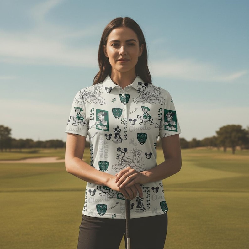 May include: White polo shirt featuring a pattern of Mickey Mouse and golf-themed graphics. The shirt has a collared neckline and short sleeves. The design includes images of Mickey Mouse, shields, and the words "Mickey Golf Classic".
