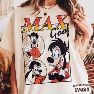 May include: Ivory-colored t-shirt featuring a graphic of Max Goof in a red hoodie. The design includes the text "MAX Goof" in an orange and yellow gradient. The shirt is labeled "COMFORT COLOR" and "IVORY".