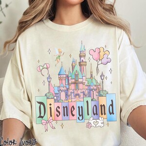Puede incluir: Camiseta color marfil con un gr&aacute;fico del castillo de Disneyland en colores pastel. El dise&ntilde;o incluye a Campanilla, globos de Mickey Mouse y la palabra "Disneyland". La camiseta tiene un corte holgado y es de material suave.