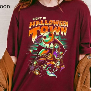 Może przedstawiać: Bordowy t-shirt z nadrukiem graficznym postaci z filmu "Koszmar przed świętami". Tekst na koszulce brzmi "Night in Halloween Town".