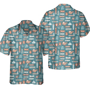 Puede incluir: Una camisa abotonada de manga corta con un fondo turquesa y un patrón repetido de gráficos naranjas y blancos. Los gráficos incluyen texto y varias ilustraciones. La camisa se muestra desde la parte delantera y trasera.