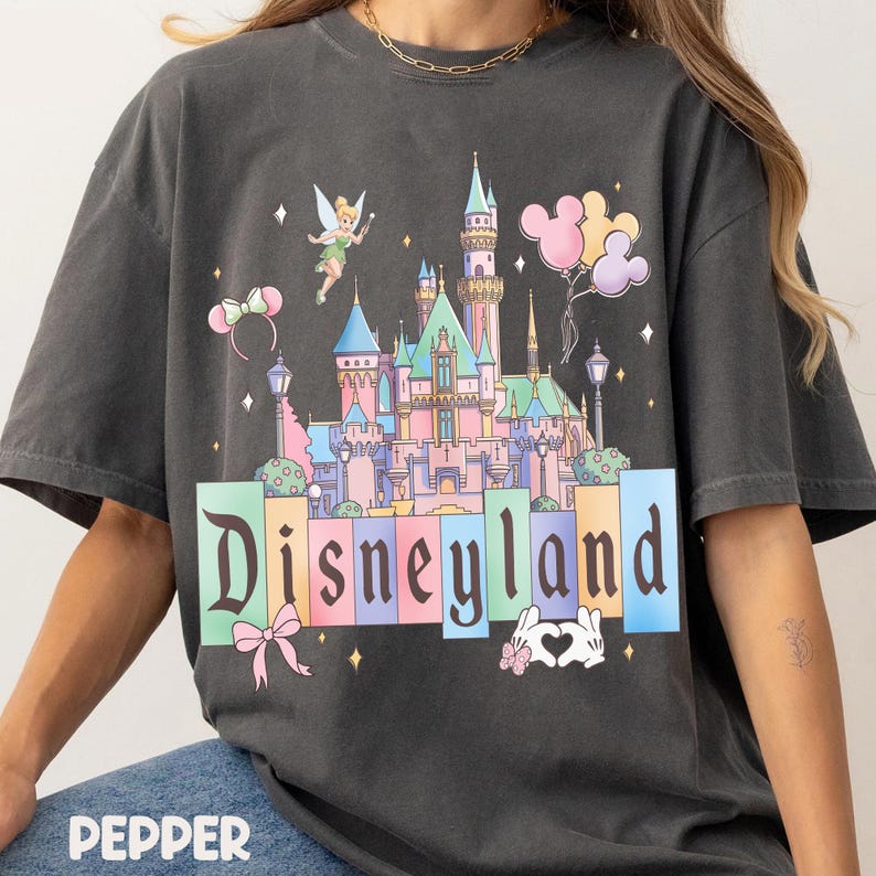 Puede incluir: Camiseta gris oscuro con un dise&ntilde;o del castillo de Disneyland, globos de Mickey Mouse y la palabra "Disneyland". El dise&ntilde;o incluye un lazo, manos de coraz&oacute;n y una diadema.