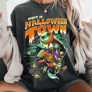 Może przedstawiać: Czarny T-shirt z nadrukiem graficznym Jacka Skellingtona z filmu "Koszmar przed świętami". Na koszulce nadrukowany jest tekst "Night in Halloween Town".