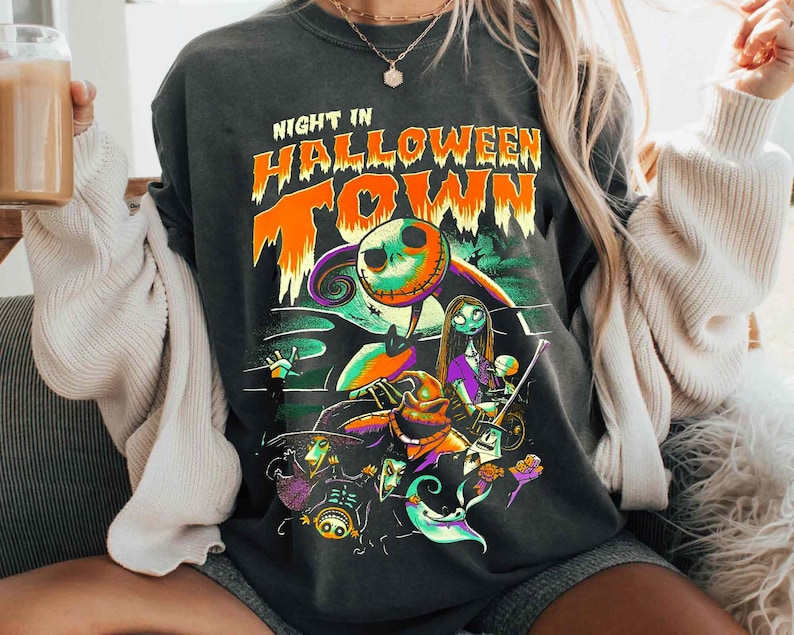 Może przedstawiać: Czarny T-shirt z nadrukiem graficznym Jacka Skellingtona z filmu "Koszmar przed świętami". Na koszulce nadrukowany jest tekst "Night in Halloween Town".