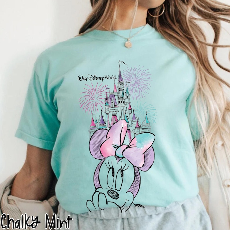 Pode incluir: Camiseta azul clara com uma ilustra&ccedil;&atilde;o da Minnie Mouse, um castelo e fogos de artif&iacute;cio. As palavras "Walt Disney World" s&atilde;o impressas acima do castelo. A camiseta tem mangas curtas e decote redondo.