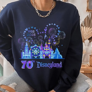 May include: A navy blue sweatshirt with a graphic of the Disneyland castle and fireworks. The text "1955 2025 70th Disneyland Resort" is printed on the sweatshirt.