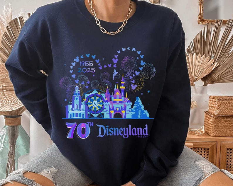 May include: A navy blue sweatshirt with a graphic of the Disneyland castle and fireworks. The text "1955 2025 70th Disneyland Resort" is printed on the sweatshirt.