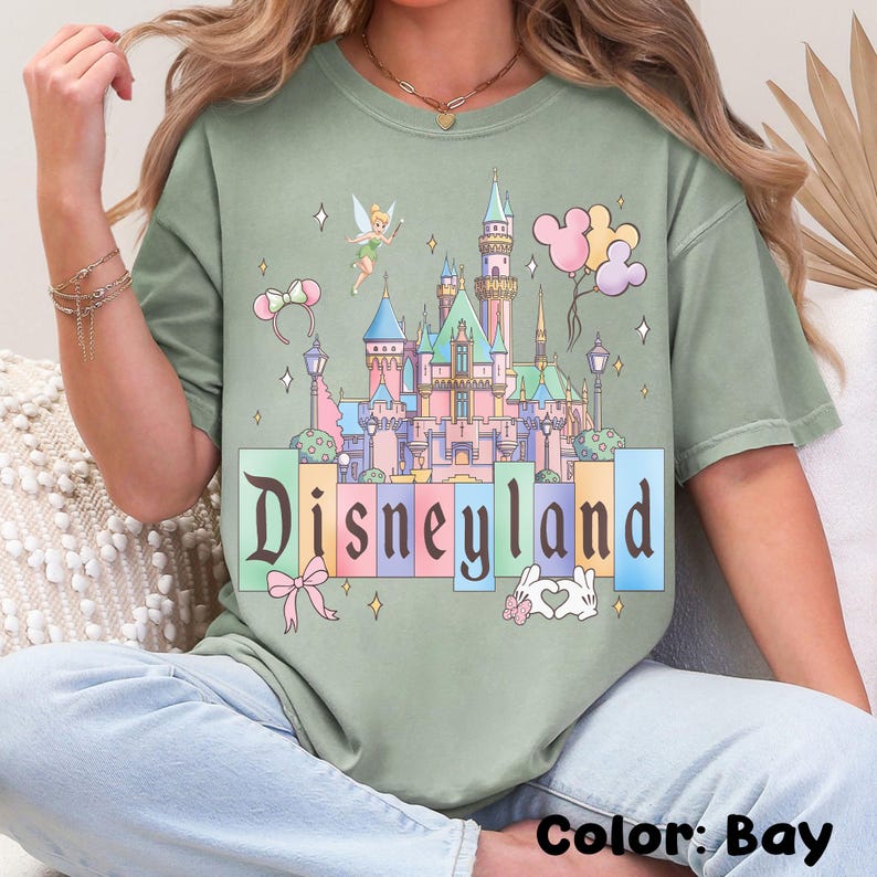 Puede incluir: Camiseta color bah&iacute;a con un gr&aacute;fico del castillo de Disneyland. El dise&ntilde;o incluye a Campanilla, globos y la palabra "Disneyland". La camiseta es de corte holgado.