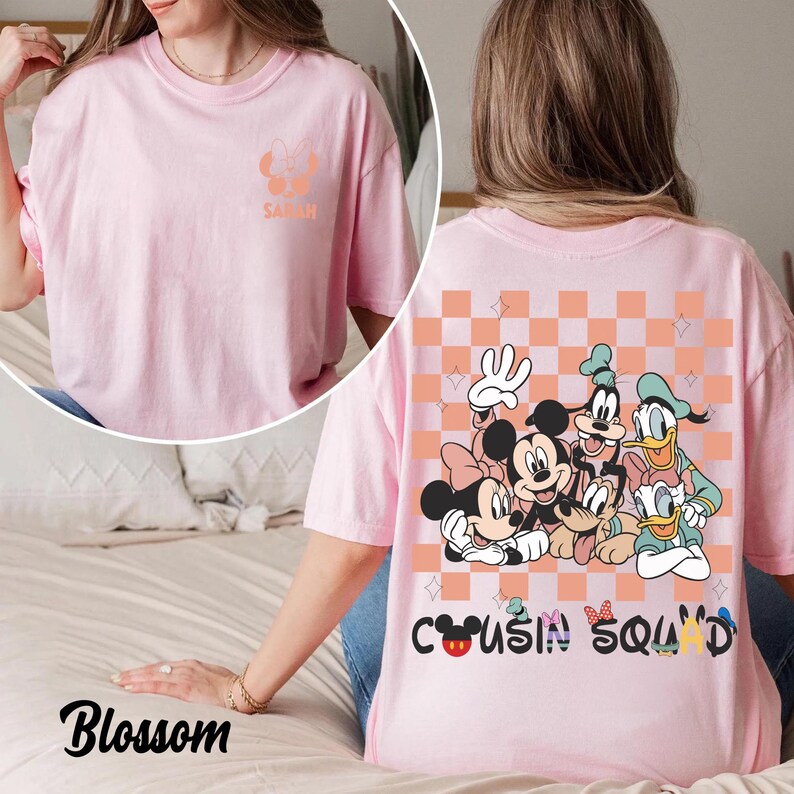 May include: Pale pink t-shirt with a Minnie Mouse design and the name "Sarah" on the front. The back features a graphic of Disney characters, including Mickey, Minnie, Goofy, and Donald Duck, with the text "Cousin Squad".