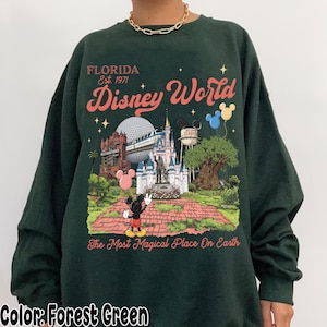 Puede incluir: Sudadera verde bosque con un dise&ntilde;o colorido de Disney World en Florida. El dise&ntilde;o incluye a Mickey Mouse, un castillo y el texto "Disney World" y "The Most Magical Place On Earth".