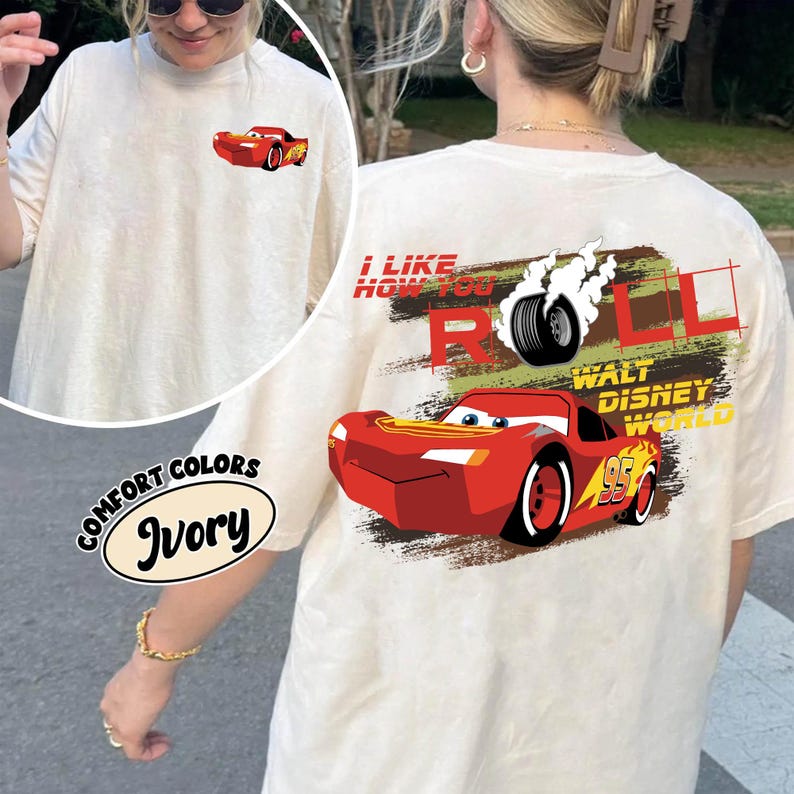 Puede incluir: Camiseta de color marfil con un coche de carreras de dibujos animados rojo en la parte delantera y trasera. El dise&ntilde;o trasero incluye el texto "I LIKE HOW YOU ROLL" y "WALT DISNEY WORLD". La camiseta est&aacute; etiquetada como "COMFORT COLORS" e "Ivory".