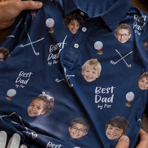 May include: Navy blue golf polo shirt with a pattern of children's faces, golf balls, and crossed golf clubs. The text "Best Dad by Par" is printed on the shirt. A golf glove and a Fairway cap are also visible.